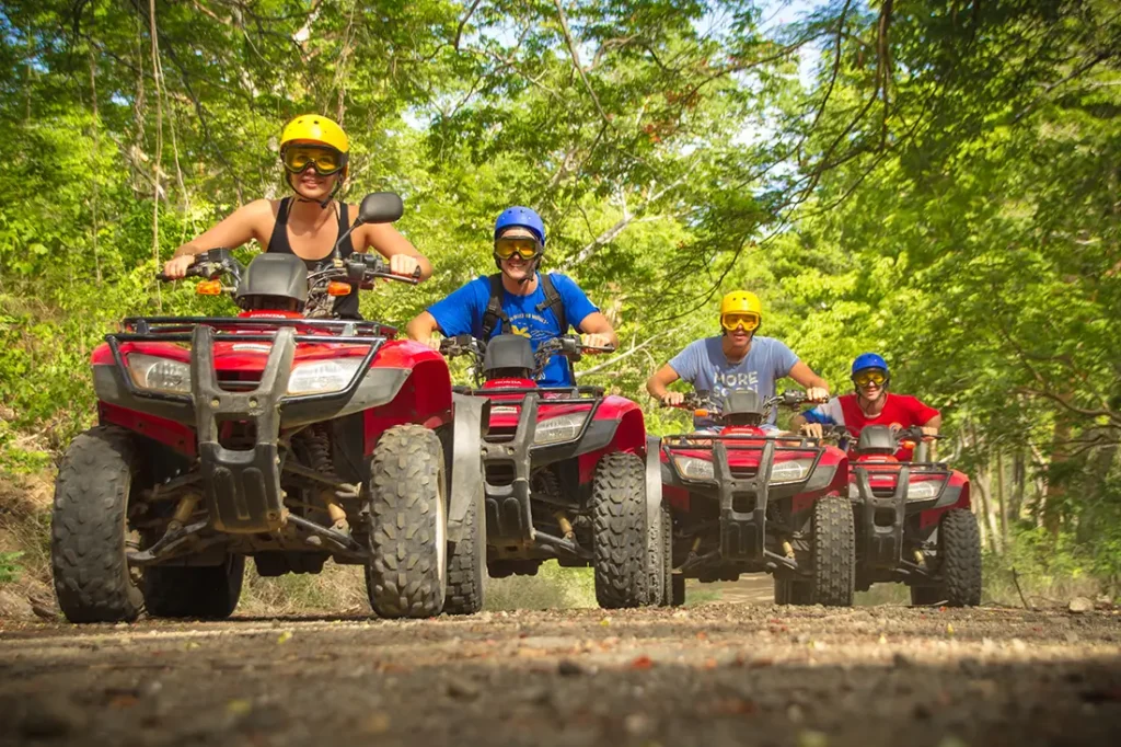 group of friends riding red ATVs along dirt path through green forest