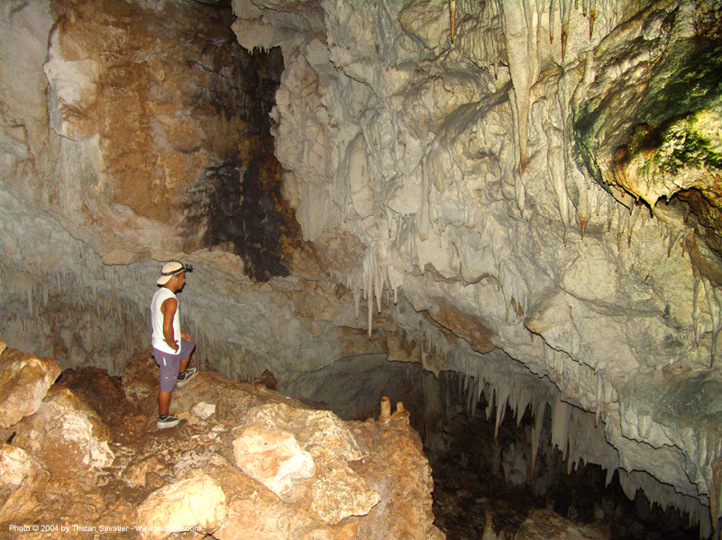Explorer standing inside large cave with stalactites and rock formations.