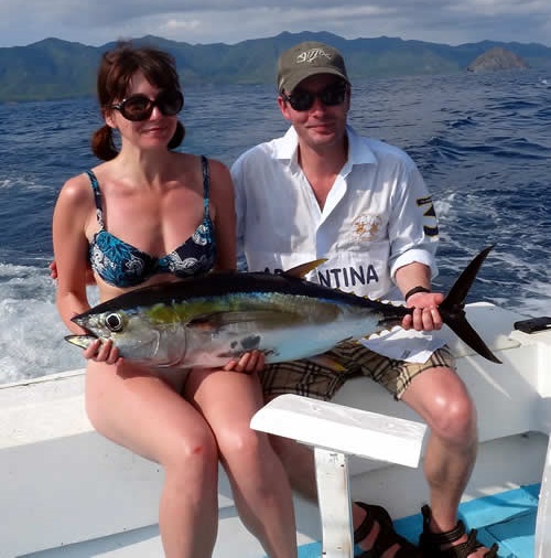 Couple holding a large tuna fish aboard a boat on the ocean.
