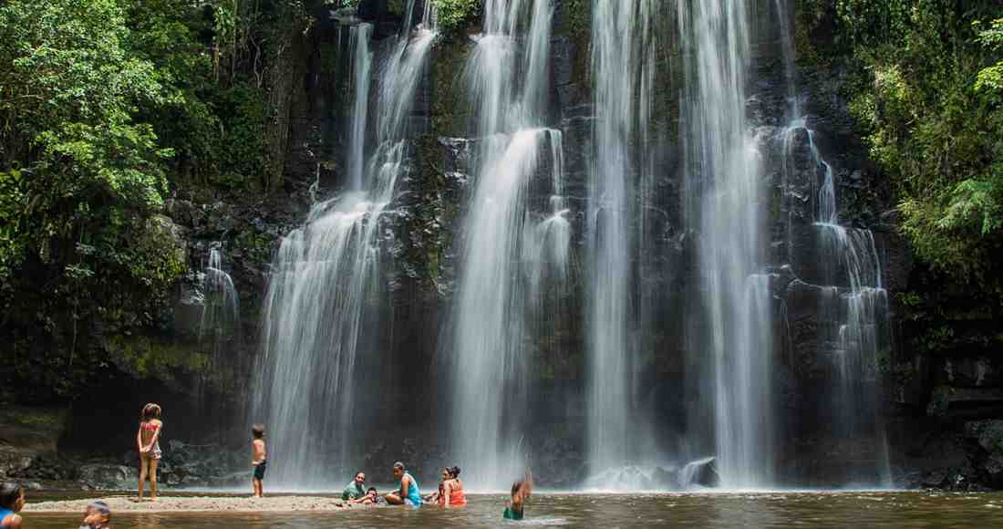 children and adults swimming near large tropical waterfall cascade
