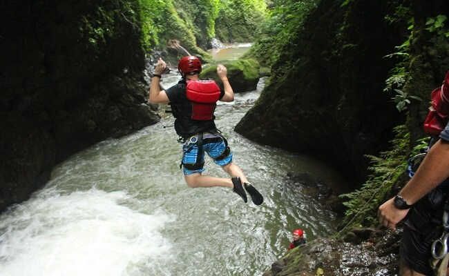 man jumping into river canyon wearing helmet and life jacket
